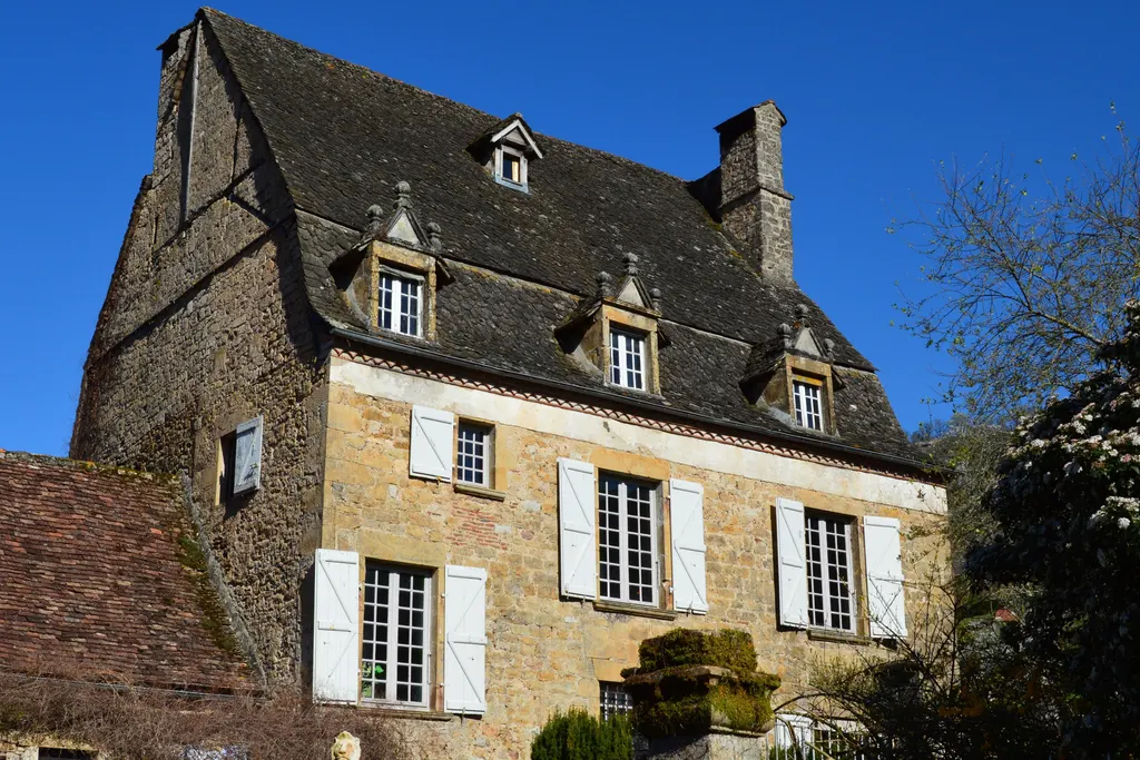 Maison de maître en pierre blonde aux volets blancs, sous un ciel bleu
